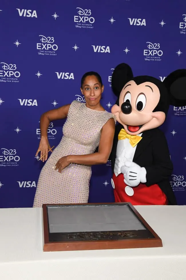 2022 Disney Legend Tracee Ellis Ross posing with Mickey Mouse. She's leaning towards him with her arms out and making a silly face. 