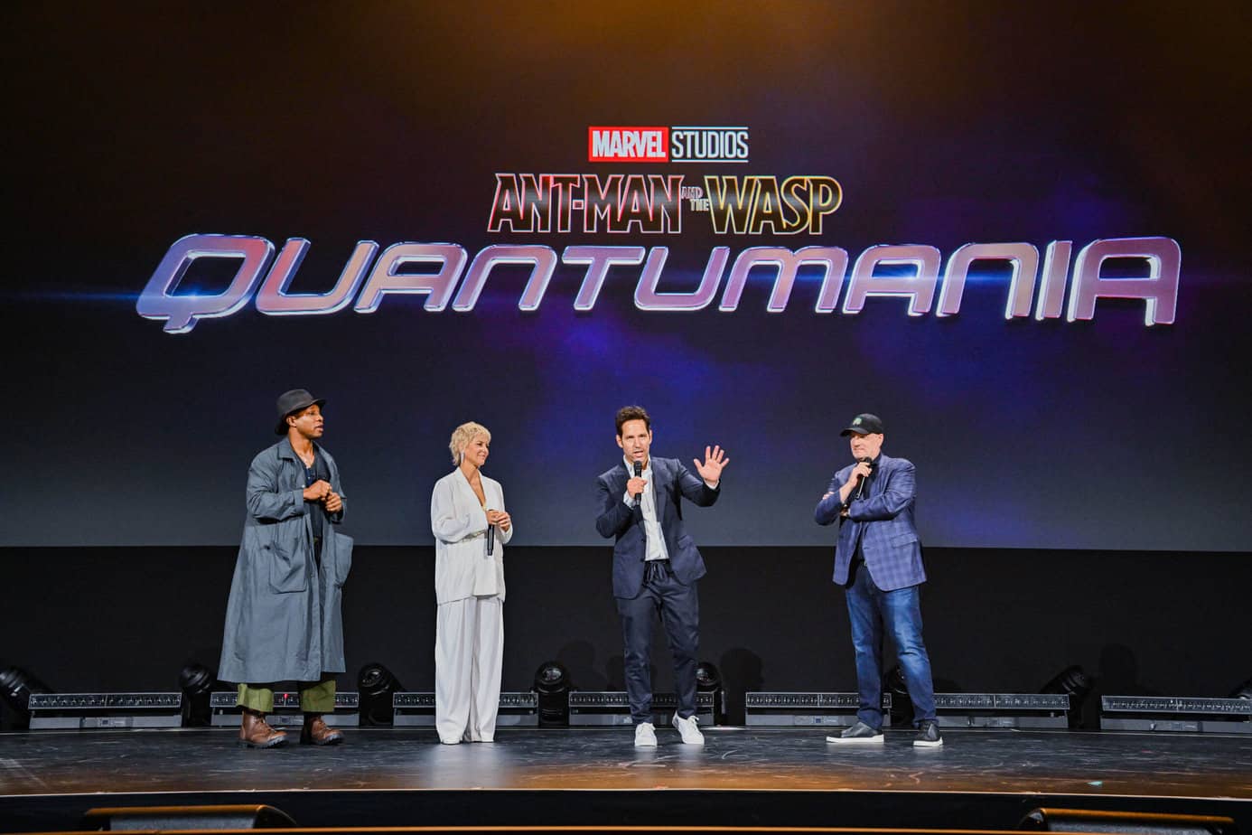 Jonathan Majors, Evangeline Lilly, and Paul Rudd on stage with Kevin Feige during the Marvel Studios panel at D23 Expo 2022 with the Ant-Man and the Wasp Quantumania logo behind them.
