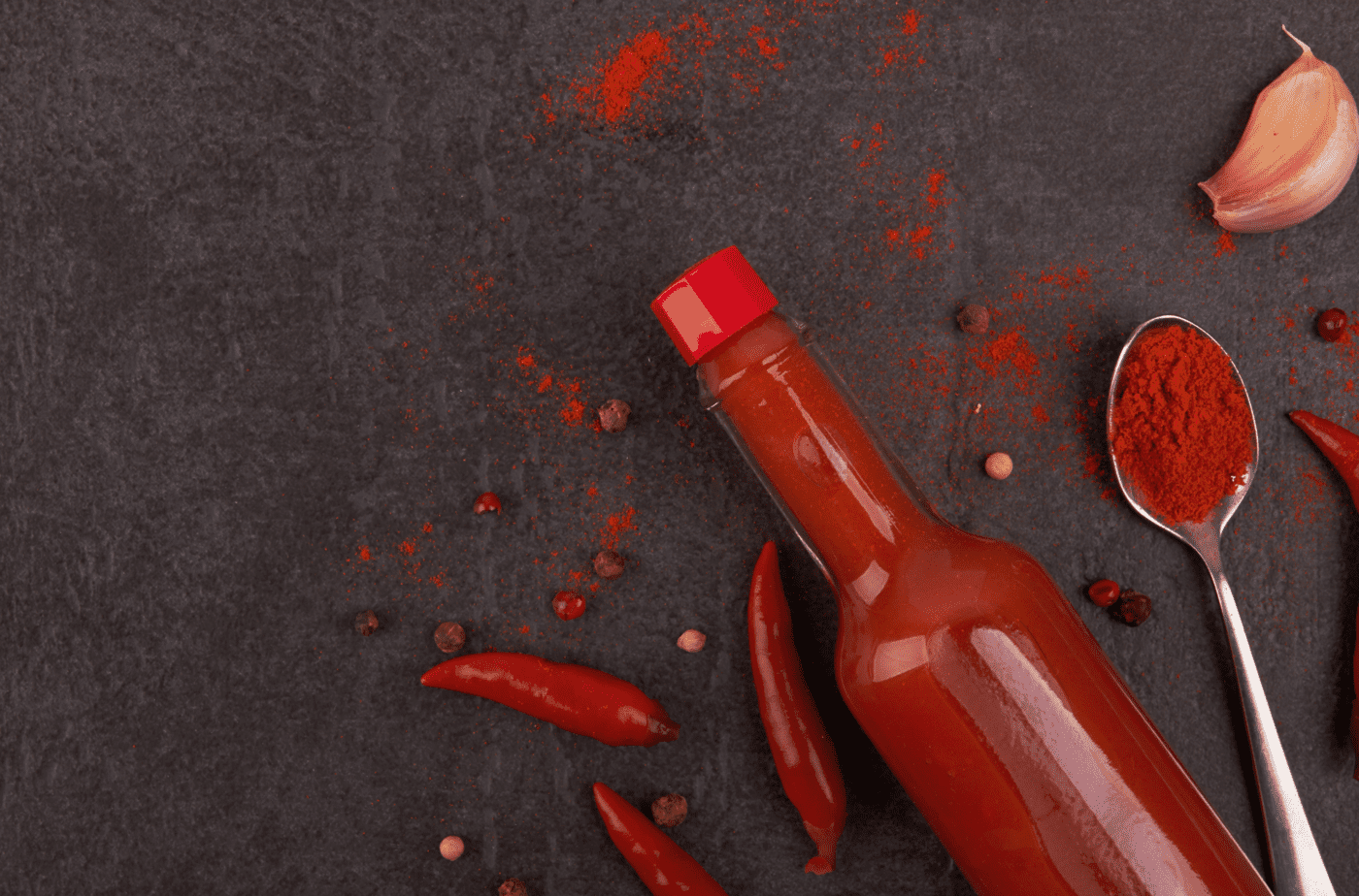 Spoilers without context glass onion hot sauce and chili powder lying on gray background